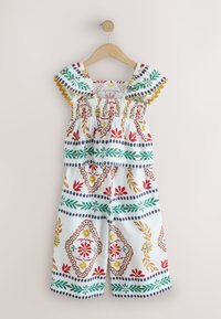 Ensemble deux pièces pour filles avec haut smocké à volants et pantalon à jambes larges, présentant des motifs floraux et géométriques colorés sur tissu blanc.