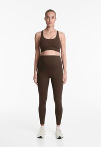 Brun sport-bh och högmidjade leggings gjorda av stretchigt material. Designen har en sömlös look och en åtsittande siluett.