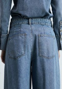 Vaaleansiniset farkut, joissa on löysä malli, kahdella takataskulla, näkyvillä ompelusaumojen yksityiskohdilla ja korkealla vyötärömallilla.