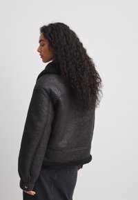 Veste en faux cuir noir avec une finition texturée et un col en polaire noir, présentant une coupe décontractée et des poignets côtelés.