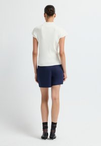 White ribbed short-sleeve top paired with navy shorts. The look features a fitted design and black shoes with sheer socks.