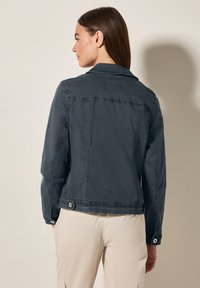 Mörk denimjacka med en strukturerad krage, ljusa sömmar och knappdetaljer. Har en figursydd passform och två knappstängningar vid midjan.