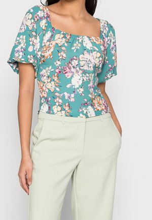 Top con stampa floreale, scollo quadrato, maniche a farfalla corte e sfondo teal. Abbinato a pantaloni a vita alta di un verde chiaro.