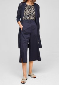 Pantalones culottes navy con aberturas laterales, combinados con una blusa beige de estampado y un cárdigan navy transparente. El calzado son sandalias grises tipo slide.