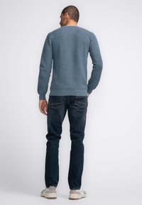 Blauwe gebreide trui met ribbelstructuur, ronde halslijn en lange mouwen, gecombineerd met donkere jeans en lichte sneakers.