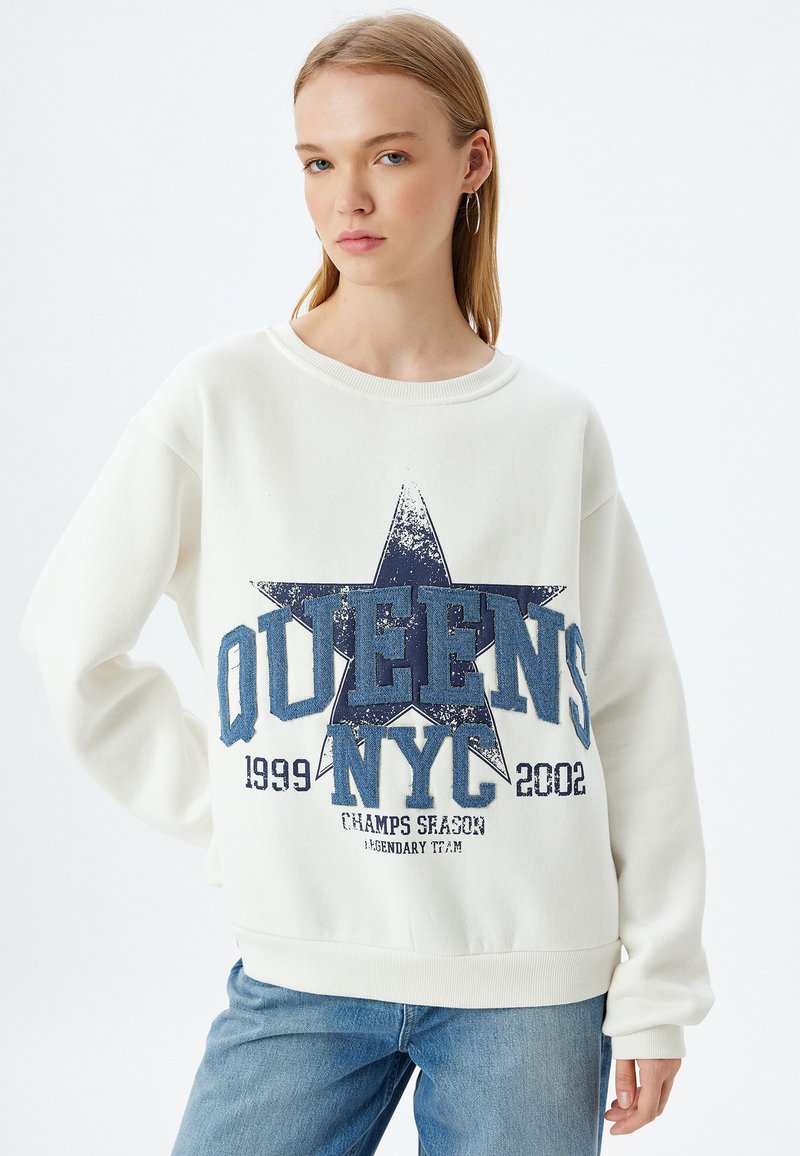 Sudadera blanca con un estampado gráfico que presenta una estrella azul y el texto "QUEEN'S NYC", con detalles texturizados y puños y dobladillo de canalé.