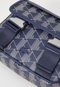 Sac bleu marine avec un motif géométrique blanc, présentant une surface texturée, des fermoirs en métal doubles et un accent de logo. Forme structurée avec des anses.