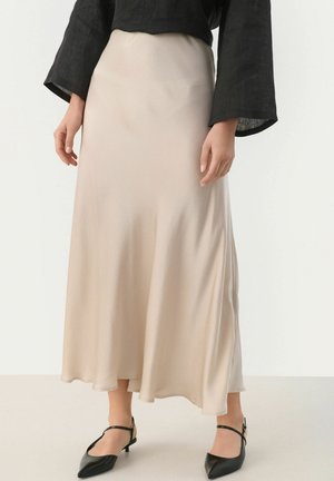 Jupe maxi en satin beige avec une texture lisse, un léger éclat et un design fluides, associée à des escarpins noirs à bout pointu et un haut noir.