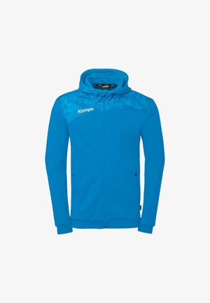 Veste à capuche bleue avec fermeture éclair intégrale, motif géométrique sur les épaules, manches longues, poches latérales et logo "Kempa" sur la poitrine.