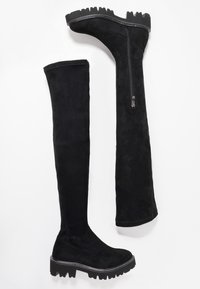 Bottes en daim noir montant au-dessus du genou avec une semelle en caoutchouc épaisse, une fermeture éclair sur le côté et des surpiqûres contrastantes le long du bord de la semelle.