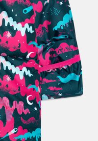 Rękaw kolorowej kurtki z abstrakcyjnymi, różowymi, turkusowymi i białymi wzorami inspirowanymi kosmosem, które zawierają gwiazdy, sierpowe księżyce i wirujące kształty.