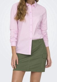 Camicia button-up a righe rosa chiaro abbinata a una gonna verde fino al ginocchio. La camicia presenta un colletto classico e chiusura con bottoni.