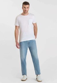 Witte katoenen T-shirt met een borstzakje, gecombineerd met lichtblauwe denim jeans met rechte pijpen. Witte sneakers maken de outfit compleet.