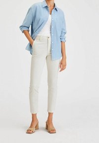 Camicia button-up azzurro chiaro, canotta bianca, pantaloni slim-fit color crema e sandali beige con tacco a blocco. Tessuto morbido con una leggera texture.