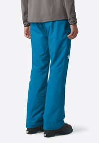 Pantaloni da sci impermeabili blu con vestibilità rilassata e tasche con cerniera. Presentano una texture liscia e fondi rinforzati. Branding discreto visibile.