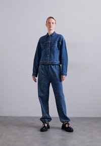 Denim jaka ar pogu priekšpusi un krūšu kabatām, apvienota ar atbilstošām biksēm ar piedurkņu siksnām. Abas ir vidēji zilā tonī un brīvā piegriezumā.