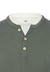 Donkergroen katoenen polo met een witte kraag, voorzien van een twee-knopenlijst en subtiele ribstructuur. Etiket toont merk- en verzorgingsdetails.