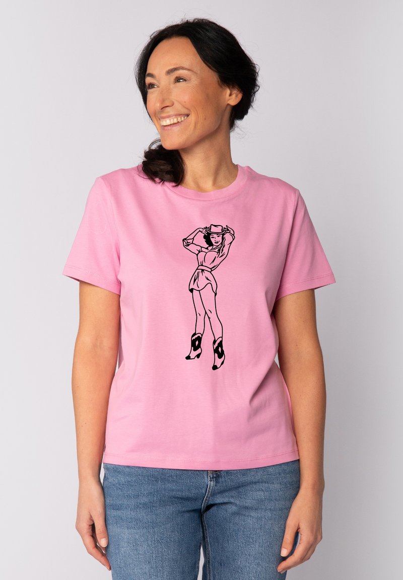 T-shirt en coton rose avec un design graphique noir représentant une femme dans une pose ludique. Manches courtes, col rond et coupe décontractée.