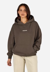 Καφέ oversized φούτερ από βαμβάκι, με μπροστινή τσέπη και λευκή επιγραφή "PEGADOR". Συνδυασμένο με υφασμένα μπεζ παντελόνια.