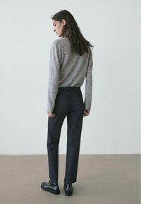 Maglione grigio lavorato a maglia, pantaloni scuri e stivali neri alla caviglia. Trame lisce, design aderente e stile minimalista. Palette di colori semplice.