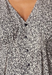 Černobílé květované šaty s výstřihem do V, nařaseným pasem a třemi černými knoflíky vpředu. Měkká, strukturovaná látka s jemným vzorem.