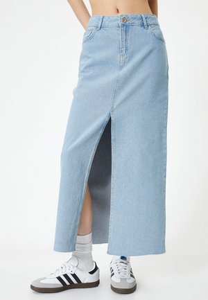 Hellblaues Denim-Maxikleid mit einem Schlitz vorne, hoher Taille und einem Reißverschluss. Kombiniert mit weißen Sneakers und gerippten Socken.