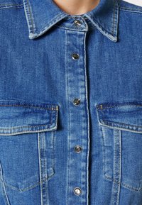 Jeansjacka i ljusblått med spetsig krage, silverfärgade tryckknappar, dubbla bröstfickor och subtila blekningar för textur.