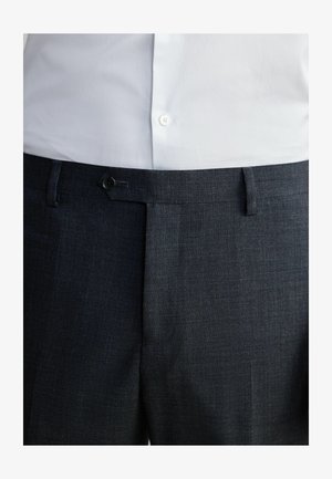 Pantaloni di tessuto grigio scuro con una superficie liscia, design a vita alta, chiusura con bottone e passanti per la cintura. Abbinati a una camicia bianca.