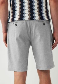 Shorts gris en tissu texturé, dotés de deux poches arrière avec boutons noirs, coupe ajustée et longueur mi-cuisse.