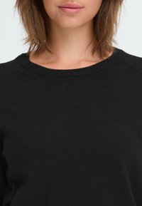 Zwarte gebreide trui met een ronde halslijn en raglanmouwen. Gladde textuur met een eenvoudige uitstraling, zonder zichtbare patronen of accenten.