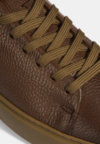 Braune Leder Sneaker mit einer strukturierten Oberfläche, ausgestattet mit geflochtenen beigen Schnürsenkeln und einer Gummisohle, die für die Freizeitgestaltung konzipiert ist.