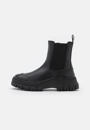 Botas Chelsea de cuero negro con paneles elásticos en los laterales, puntera redondeada y suela de goma gruesa con un patrón de relieve y una lengüeta.