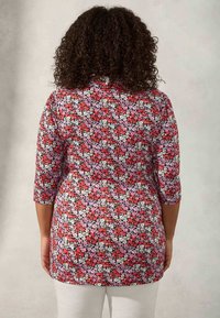 Tunika floreale con sfondo nero e fiori rossi, rosa e bianchi, maniche a tre quarti e vestibilità comoda.