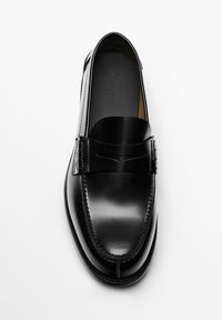 Sort lædersko uden snørebånd med en glat finish, udstyret med en dekorativ rem og diskrete syninger langs kanterne. Ingen synligt mærke.