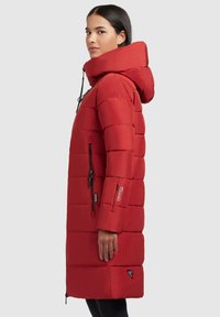 Rode pufferjas met een lang ontwerp, grote capuchon en ritszakken. Beschikt over een gestikt patroon en contrasterende hardwareaccenten.
