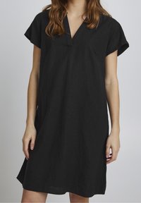 Abito in lino nero con scollatura a V, maniche corte e vestibilità rilassata. Presenta una texture sottile e arriva appena sopra al ginocchio.