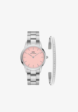 Srebrni sat od nehrđajućeg čelika s okruglim kućištem i ružičastim brojčanikom. Ima srebrne indeksne oznake, logotip i metalnu narukvicu u odgovarajućoj boji.