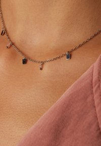 Collier en chaîne argentée avec de petits pendentifs rectangulaires et ronds, présentant des surfaces polies et un design délicat et texturé.