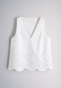 White sleeveless V-neck top with floral cut-out embroidery along the scalloped hem, displayed on a plain light background.