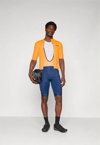 Cyklistický outfit obsahuje oranžový dres s krátkym rukávom, biele sieťované tričko, modré šortky a čiernu helmu. Súčasťou sú aj čierne cyklistické topánky.