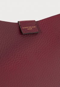 Borsa in pelle bordeaux con texture a granulato, caratterizzata da una patta cucita e un'etichetta in oro con la scritta "GIANNI CHIARINI FIRENZE."