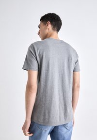 Camiseta de algodón gris con mangas cortas y escote redondo, que presenta una textura suave y un diseño sencillo y sin adornos.