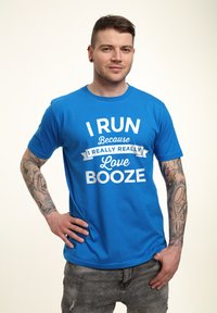 Blå bomulds t-shirt med hvid tekst, der læser "JEG LØBER Fordi jeg virkelig virkelig elsker ØL." Kortærmet og med rund hals.