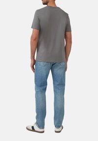Szary t-shirt z krótkim rękawem zestawiony z jasnoniebieskimi dżinsami z przetarciami oraz białymi sneakersami z czarnymi akcentami, widok z tyłu.