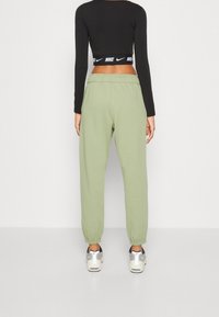 Svart långärmad croppad topp med ett midjeband med Nike-logotyp, i kombination med ljusgröna joggers med elastiska manschetter och en avslappnad passform.