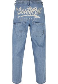 Jean en denim bleu clair avec deux poches arrière et grand texte blanc « Southpole Originals Established New York City » au-dessus des poches.