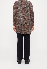 Långärmad topp med leopardmönster och rundad nederkant, kombinerad med svarta utsvängda byxor och platåstövlar, vilket framhäver olika texturer.