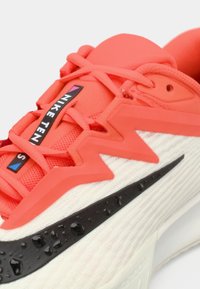 Αθλητικά παπούτσια Nike με υφασμένο κόκκινο επάνω μέρος, μαύρες γόμας λεπτομέρειες και λευκή σόλα. Εμφανείς γεωμετρικά σχεδιαστικά στοιχεία και σύστημα κορδονιών.