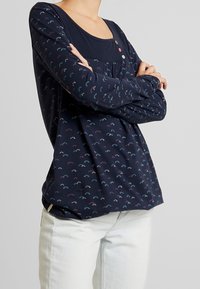 Marinblå långärmad topp med rund halsringning, prydd med ett mönster av färgglada fläktformer och dekorativa knappar vid bröstet.