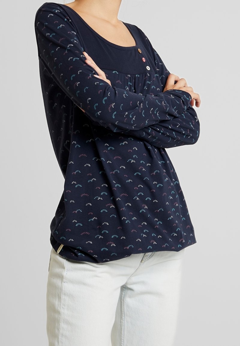 Marinblå långärmad topp med rund halsringning, prydd med ett mönster av färgglada fläktformer och dekorativa knappar vid bröstet.